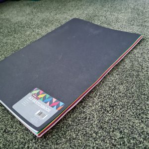 large black scrapbook with colourful pages showing at edges, lying on a green carpet