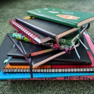 pile of multi coloured and different size and shared notebooks, lying on a green carpet
