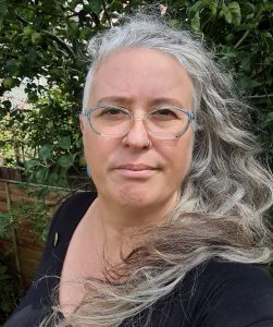 woman with long grey hair tumbling over her shoulder, with a direct open expression, looking straight into the camera